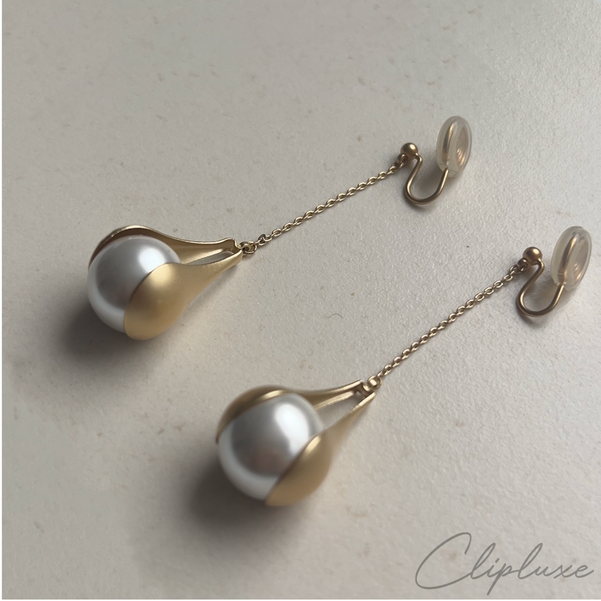 Pair of gold and pearl drop earrings on a light background with 'Cliplune' branding.