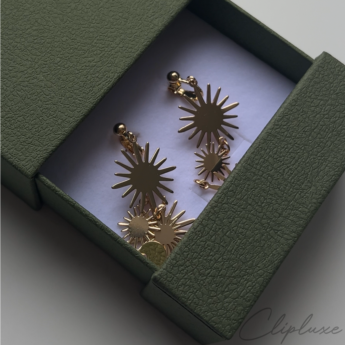 A pair of vintage gold-plated, chunky, irregular, hammered clip-on earrings for women, displayed in an open green jewelry box.