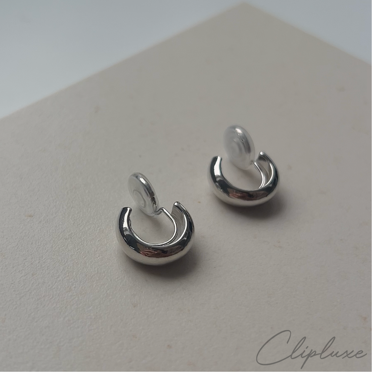 A pair of minimalistic small hoop clip-on earrings in silver color, displayed on a neutral background.